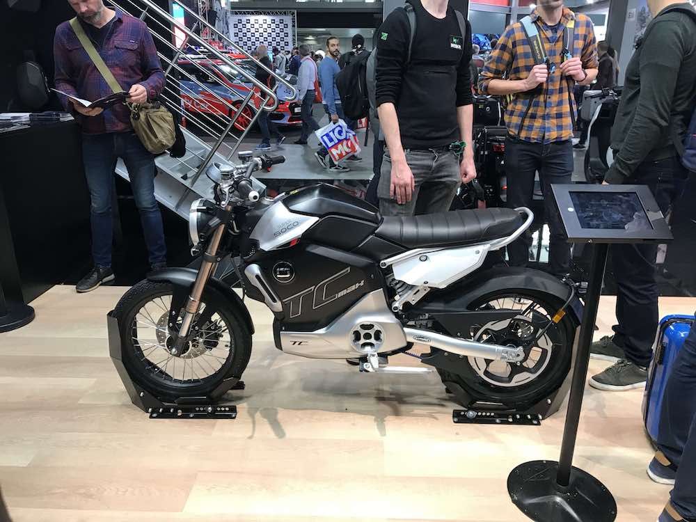  HOME GADGET MOTORI  Le migliori moto elettriche di Eicma 2019  SFOGLIA GALLERY 15 IMMAGINI Siamo andati alla fiera milanese a scoprire le novità più elettrizzanti. Ecco la nostra classifica L’edizione 2019 di Eicma, la fiera milanese dedicata alle due ruote, la conferma come una delle manifestazioni più importanti a livello mondiale. La rivoluzione elettrica nelle moto è ancora più nelle parole che nei fatti, ma inevitabilmente il motociclista moderno è cambiato e, oltre a essere esigente in termini di prestazioni, è anche interessato alla tecnologia, che ormai è diventata una discriminante di acquisto. La nostra Eicma 2019 inizia quindi con la rassegna delle moto e degli scooter elettrici; in questo articolo vi parleremo di quelli che ci hanno colpito di più.  Vespa Elettrica  Sì, è vero, probabilmente ci sono scooter della concorrenza asiatica che hanno un rapporto qualità/prezzo migliore, tuttavia, la Vespa è sempre la Vespa. Stiamo parlano del design industriale più famoso al mondo, di un’icona dell’italianità nel mondo. Ecco perché abbiamo ritenuto opportuno iniziare proprio con la Vespa Elettrica.     A Eicma ha debuttato la nuova versione in grado di raggiungere la velocità massima di 70 km/h (ora omologata come motociclo), che affianca la versione originale da 45 km/h, nata per un utilizzo prettamente urbano e perciò omologata come ciclomotore. La “nuova” Vespa in realtà come novità ha solo l’aggiornamento del powertrain, che è stato ottimizzato. Le maggiori prestazioni non incidono sull’accelerazione e sull’autonomia; quest’ultima rimane pressoché invariata e in modalità eco, con velocità limitata a 45 km/h, la Vespa Elettrica 70 km/h garantisce un’autonomia di 100 km, mentre in modalità Power è possibile percorrere fino a 70 km.  La Vespa Elettrica 70 km/h si distingue per alcuni dettagli stilistici specifici come la molla dell’ammortizzatore anteriore verniciata di rosso, tinta che viene ripresa anche sui fregi presenti sulla cover della Power Unit e sulla targhetta “Elettrica”.  Verge Motorcycles TS  In origine l’azienda finlandese si chiamava RMK Vehicles, poi la decisione di cambiare nome in Verge Motorcycles e di lanciare proprio a Eicma la versione definitiva della moto elettrica TS. Se l’estetica può risultare audace, la tecnologia è decisamente avanzata, quasi fantascientifica. Infatti, la Verge impiega la soluzione della ruota posteriore che ruota su se stessa, poiché il motore è nascosto all’interno del cerchio della ruota posteriore.  L’audace ruota-motore è alimentata dai cavi arancione ad alta potenza; questa soluzione ha consentito all’azienda finlandese di evitare l’utilizzo di tutta la meccanica che trasferisce potenza alla moto, come la catena o la cinghia. Le prestazioni sono interessanti: potenza di 80 kW, coppia di 1.000 Nm e autonomia che varia da 200 (in autostrada) a 300 km (in città) a seconda dell’ambito e della tipologia di utilizzo. Attualmente è possibile prenotare la moto versando una caparra di 2mila euro; il costo finale dovrebbe aggirarsi intorno ai 25mila euro (più le tasse).  Kymco RevoNEX  Della moto elettrica presentata in anteprima dalla Kymco sappiamo molto poco, ma quel poco che sappiamo ci basta per sognare. Estetica da dura naked, coda rastremata e cambio manuale a sei marce. Sì, avete letto bene, la Kymco ha pensato bene di restituire al suo pubblico una moto bella e piacevole da guida e con un allungo simile a quello delle endotermiche. Le quattro modalità di guida dovrebbero consentire una gestione oculata dell’autonomia. Notevoli le prestazioni: da 0 a 100 km/h in 3,9 secondi, e da 0 alla velocità massima, pari a 205 km/h, in 11,8 secondi. Grazie al sistema Active Acoustic Motor, la moto sarà in grado di riprodurre il rumore di un motore normale. Arriverà nel 2021.  Kymco i-One DX  È uno scooter perfetto per la città: è piccolo e maneggevole. Dotato di due batterie agli ioni di litio rimovibili, che consentono un’autonomia di 90 km con velocità di 30 km/h, e una punta di 74 km/h, l’i-One DX presenta un’estetica molto curata grazie alle luci a led e agli indicatori di direzioni animati. Sullo scooter c’è il sistema multimediale proprietario Noodoe.  Zero Motorcycles SR/F  La Zero Motorcycles è un’azienda americana nata 13 anni fa con l’obiettivo di fare “vere” moto elettriche. E nel tempo c’è riuscita. La SR/F portata all’Eicma è una moto che trasmette una sensazione di sicurezza solo a guardarla; è equilibrata, per nulla eccessiva e, soprattutto, tanto veloce. La velocità di punta è infatti 200 km/h e l’autonomia di 320 km.  Super Soco  Super Soco TCmax2